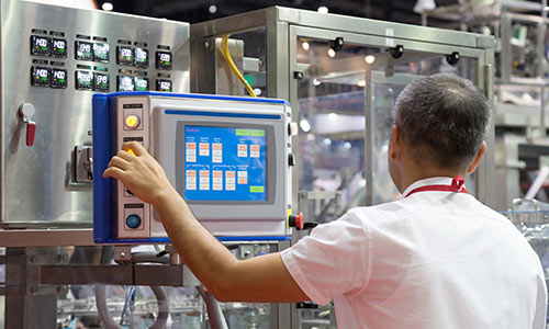 A worker in a manufacturing facility is pressing a button on a machine's interface.