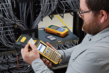 A man using LinkWare Live and a portable printer to organize a complex cable array.