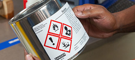 A person applies a GHS label to a metal can.