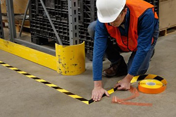 A worker marking an area of a manufacturing factility with yellow and black stiped tape.