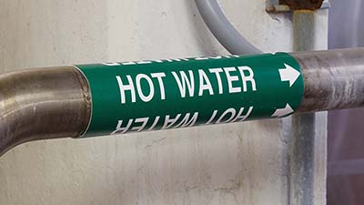 A green pipe marker that says 'Hot water.'