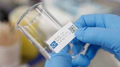 A person attaches a QR code label to a beaker.