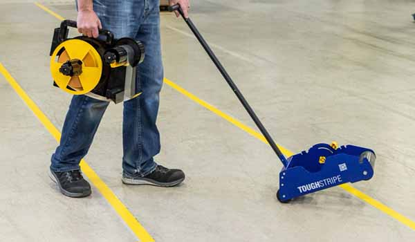 A contractor walks across a polished concrete floor, pushing a tape applicator.