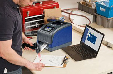 A man working at a desktop with a Brady printer and a laptop.