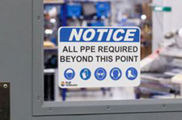 A sign on a door window that says "NOTICE ALL PPE REQUIRED BEYOND THIS POINT."