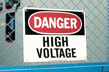 A sign that says "DANGER HIGH VOLTAGE" on a chain link fence.