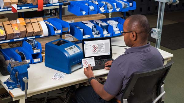 A worker designs and prints a GHS label using Brady's Workstation software and a BBP30 label printer.