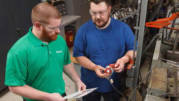Two men discussing lockout tagout procedures on a piece of cutting machinery in a warehouse setting.