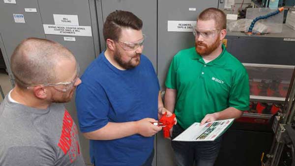 Three men discussing lockout tagout procedures while holding a valve lockout device.