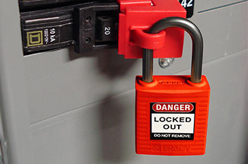 A padlock locked to a lockout tagout device that is blocking access to an electrical breaker.