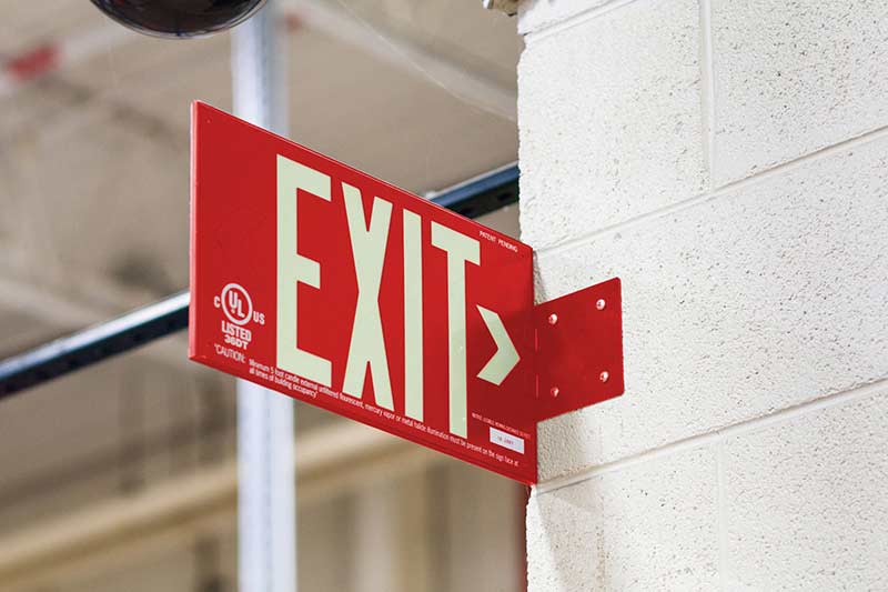 A red exit sign hangs on a concrete warehouse wall.
