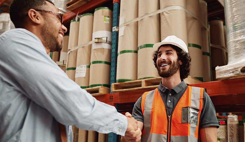 A manager welcomes his new employee in an industrial warehouse environment.