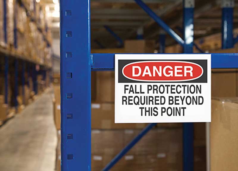 A fall protection is required sign located on storage racks in an industrial warehouse.