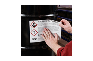 A person applying a hazardous material label to the side of a container.