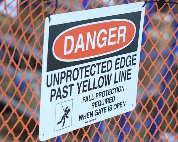 A view of a fence with an OSHA Danger sign that says 'Danger - Unprotected Edge Past Yellow Line - Fall Protection Required When Gate is Open.'