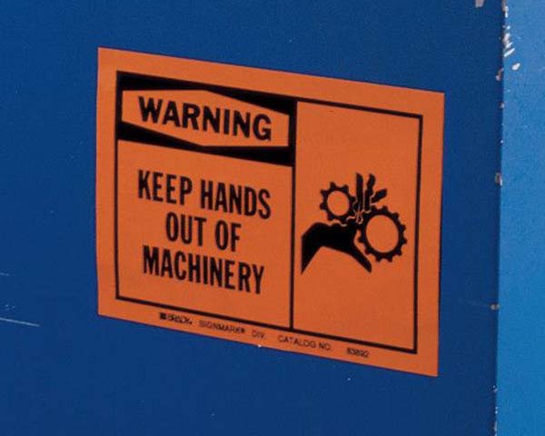 An orange electrical safety sign that says 'Warning - Keep Hands Out of Machinery' is displayed on a large, blue industrial piece of equipment.'
