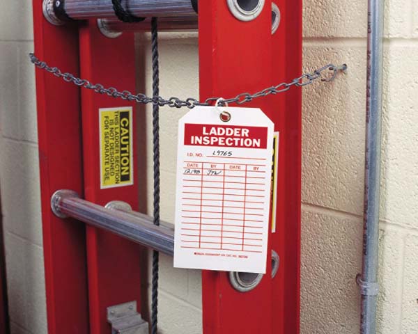 A ladder inspection safety tag hangs on a red ladder in a workplace environment.