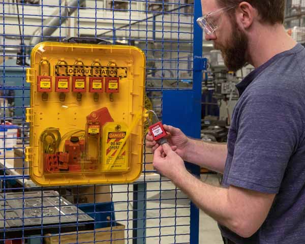A man unlocking a lockout padlock that's attached to a yellow lockout station in a warehouse environment.