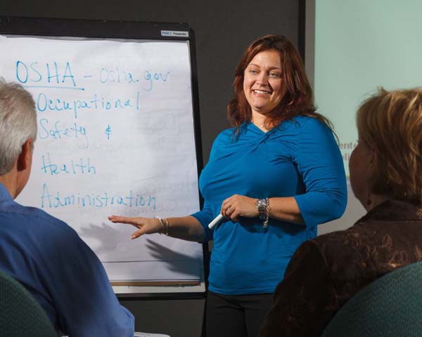 A woman provides OSHA training to a room of employees in a conference room.