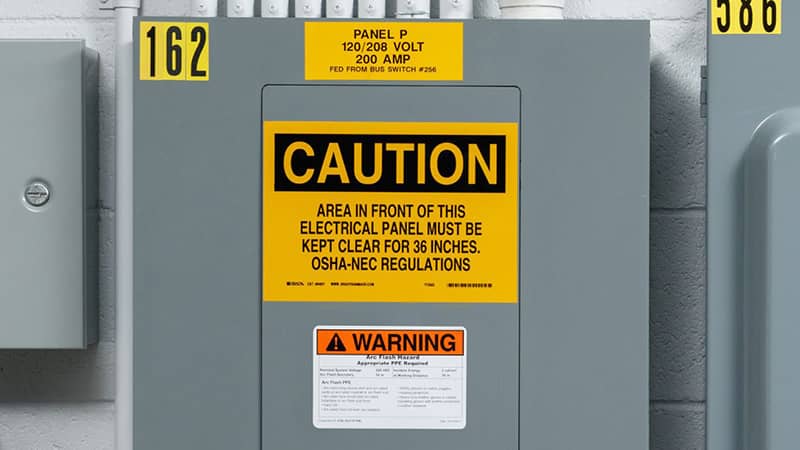 Safety signage on an electrical panel warning users of arc flash risks and regulatory requirements.