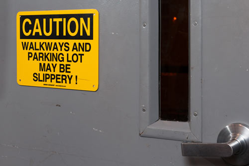 Example of a caution sign on a door. It says 'Caution: Walkways and parking lot may be slippery!'