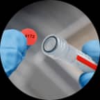 A red label with printed text being applied to the top of a tube with a corresponding color.