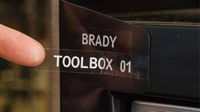 A Brady clear polyester label with the text Toolbox 01 being applied to a toolbox.
