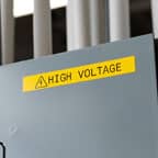 A large yellow Brady label with the text "High Voltage" applied to an electrical panel.