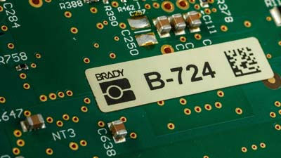 A white label on a circuit board with a logo, id and 2D barcode.