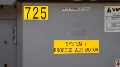 Two yellow Brady all-weather reflective labels applied to the side of a equipment box to identify its unit number and purpose.