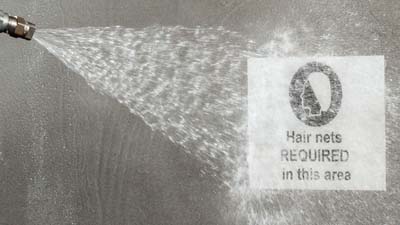 A worker using a water-jet spray to clean a Brady toughwash metal detectable label that is applied to a piece of machinery.