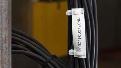 A white non-adhesive polyethylene tag with printed text attached to a wire that is part of a larger bundle of wires.