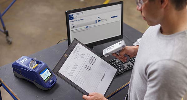 A man is scanning a label with a handheld device. The data from the label appears instantly on a computer screen in front of him.